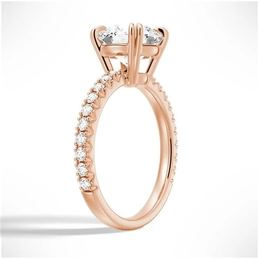 Angled view of Classic Round Moissanite Solitaire Engagement Ring 4 Prong with Pave Band in Rose Gold - Novelle Vow