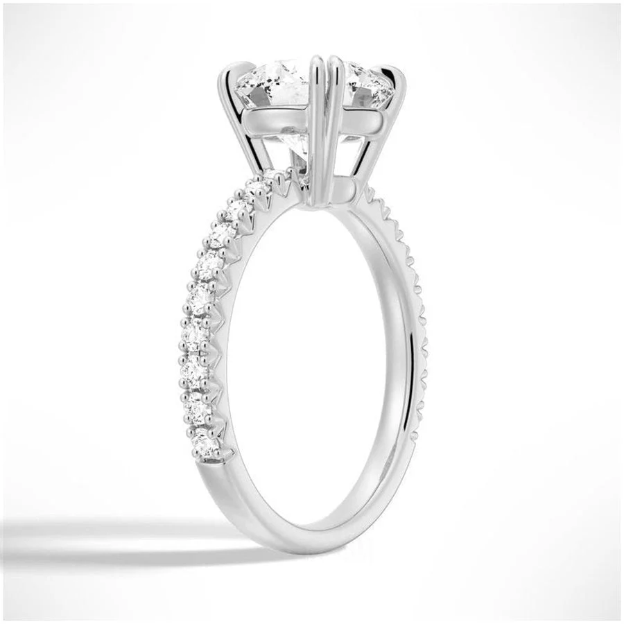Angled view of Classic Round Moissanite Solitaire Engagement Ring 4 Prong with Pave Band in White Gold - Novelle Vow