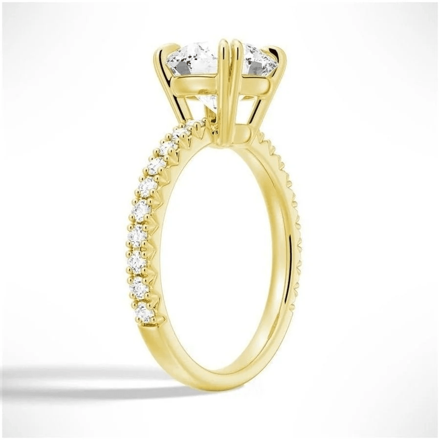 Angled view of Classic Round Moissanite Solitaire Engagement Ring 4 Prong with Pave Band in Yellow Gold - Novelle Vow