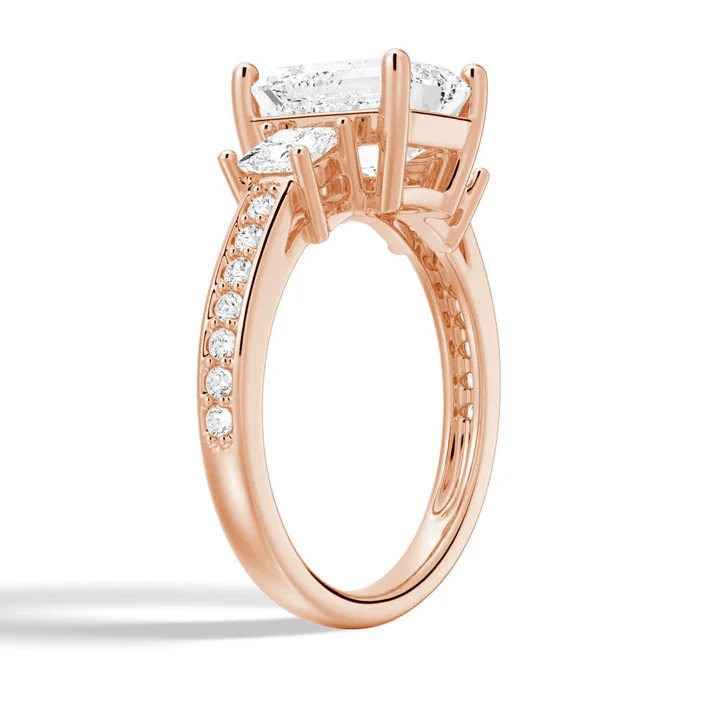 Angled profile view of Emerald Cut Three Stone Moissanite Engagement Ring with Pave Band in Rose Gold - Novelle Vow