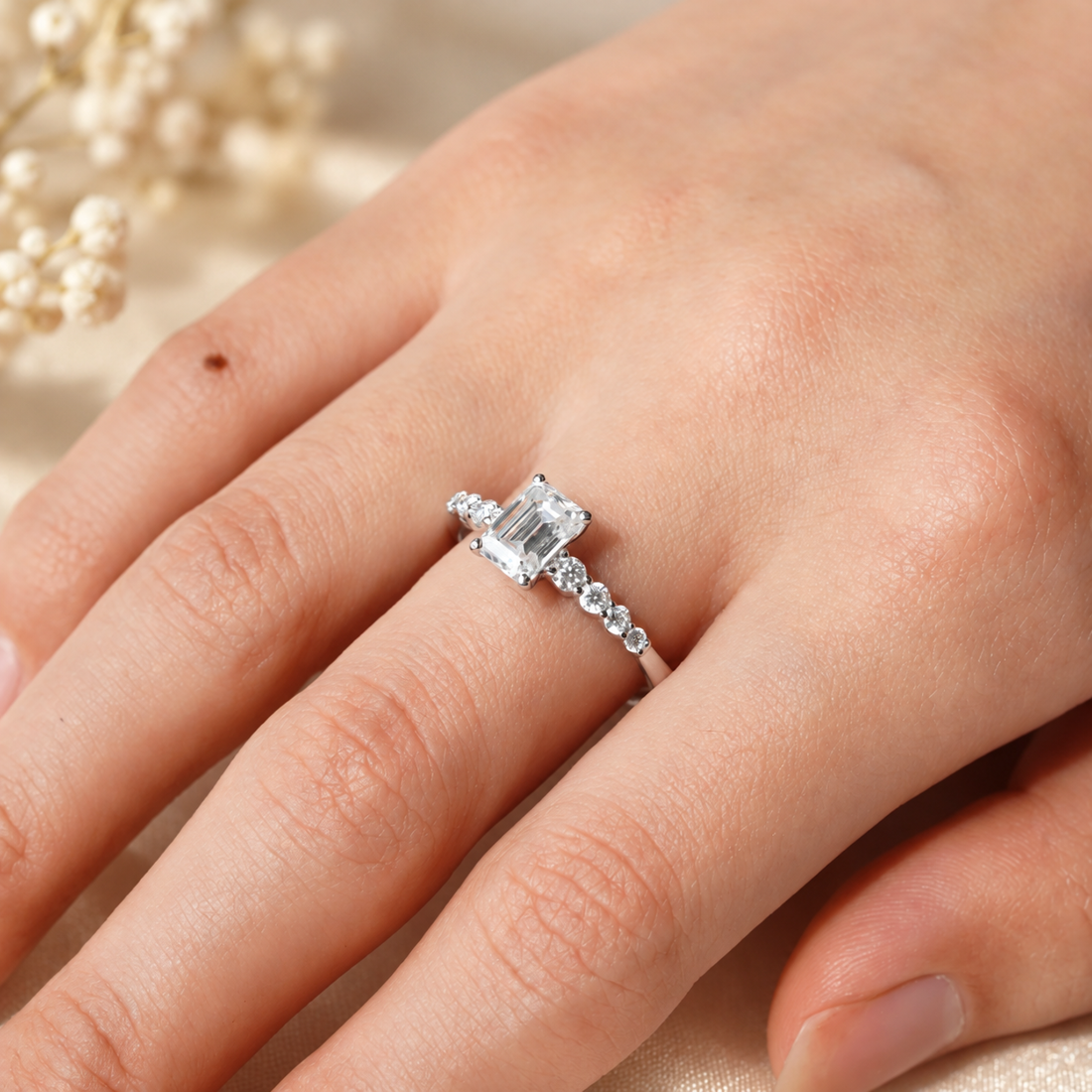 White gold emerald cut moissanite shared-prong engagement ring worn on model finger close up