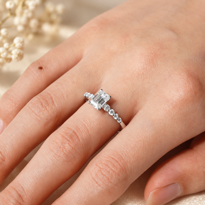 White gold emerald cut moissanite shared-prong engagement ring worn on model finger close up