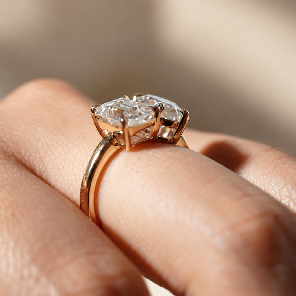 Rose gold emerald and pear cut toi et moi moissanite engagement ring on model finger top view