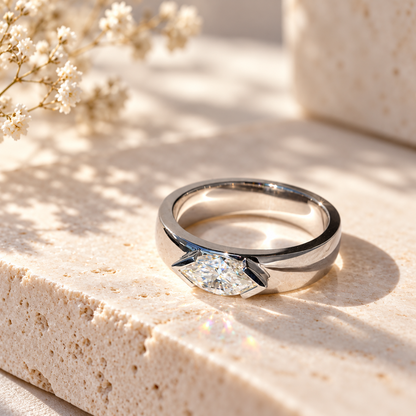White gold marquise cut moissanite east-west half bezel solitaire ring resting on travertine stone in sunlight