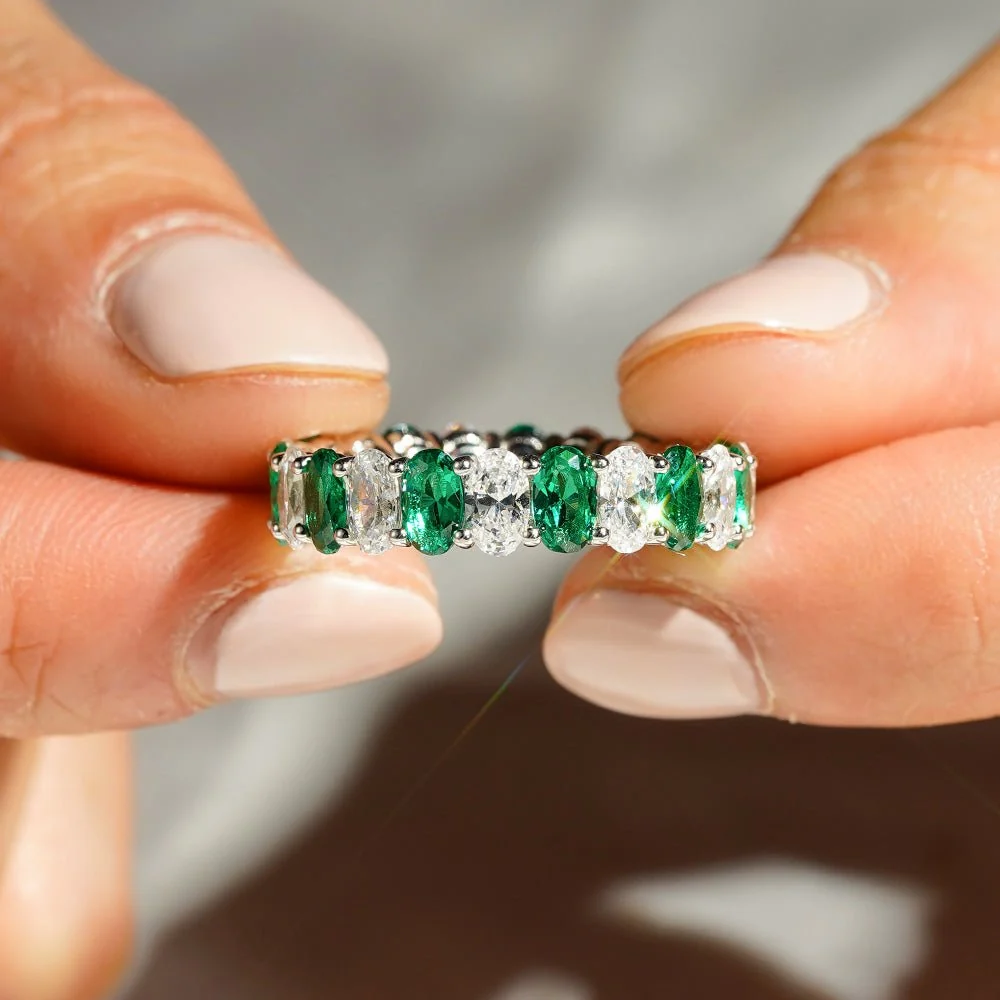 Close-up view of hands holding 5mm oval lab grown emerald and white sapphire eternity band