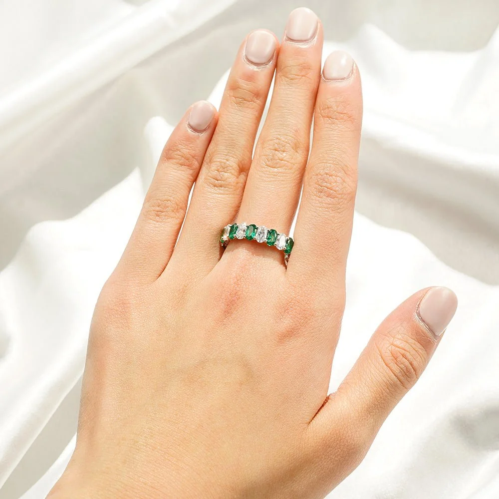 On-model hand view wearing oval lab grown emerald and white sapphire ring on silk background