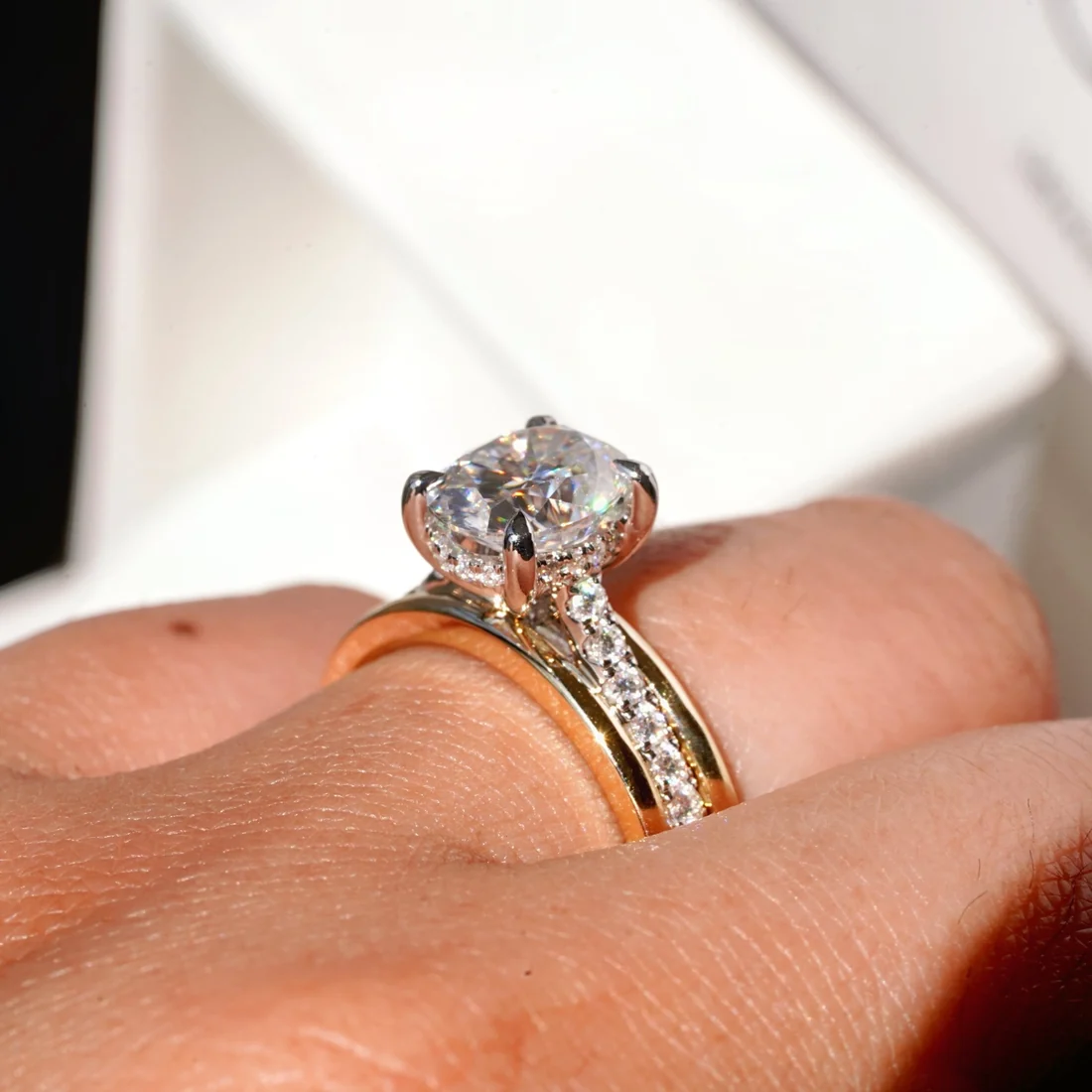 Close-up view of model wearing two-tone gold oval moissanite engagement ring with hidden halo