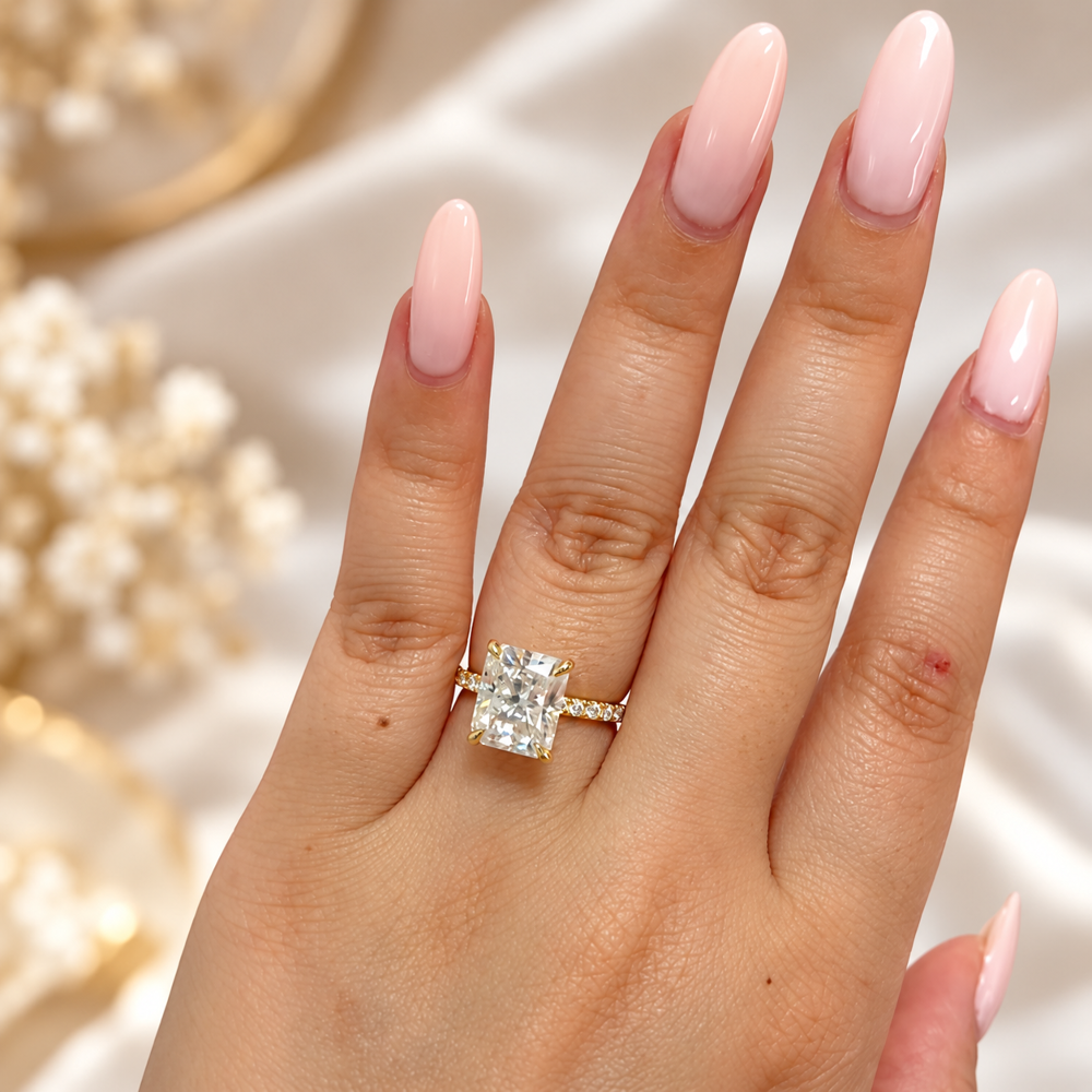 Yellow gold 5ct radiant cut moissanite engagement ring with pave band worn on model hand
