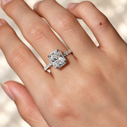 White gold radiant cut moissanite halo engagement ring with pave band worn on model finger