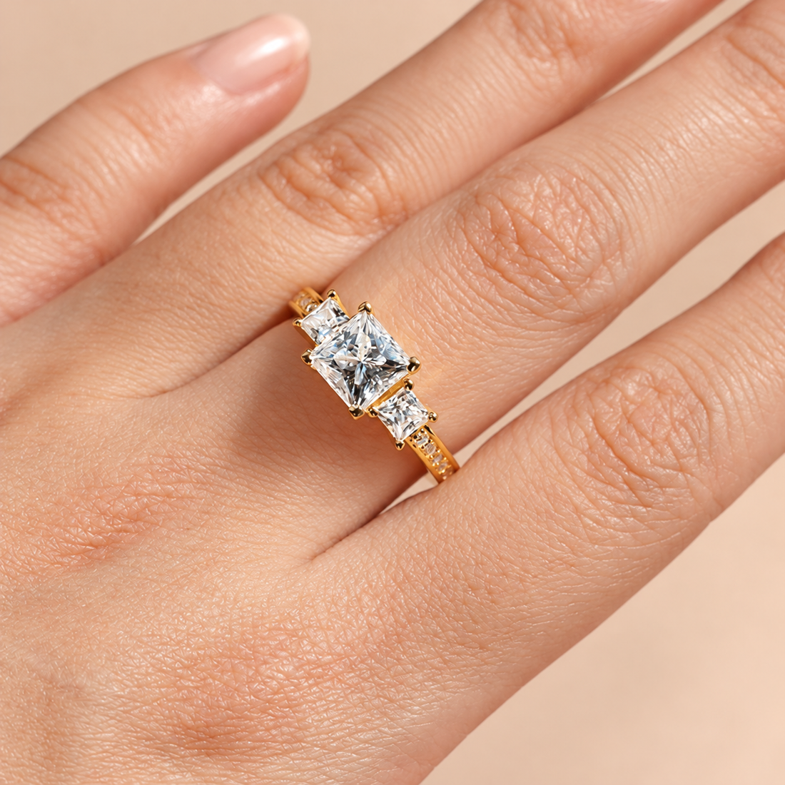 Close-up view of model wearing yellow gold three-stone princess-cut moissanite engagement ring on hand
