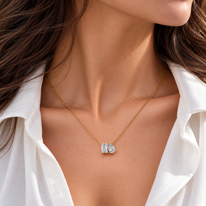 Yellow gold Toi et Moi emerald cut and pear shaped moissanite two stone pendant necklace worn on model collarbone